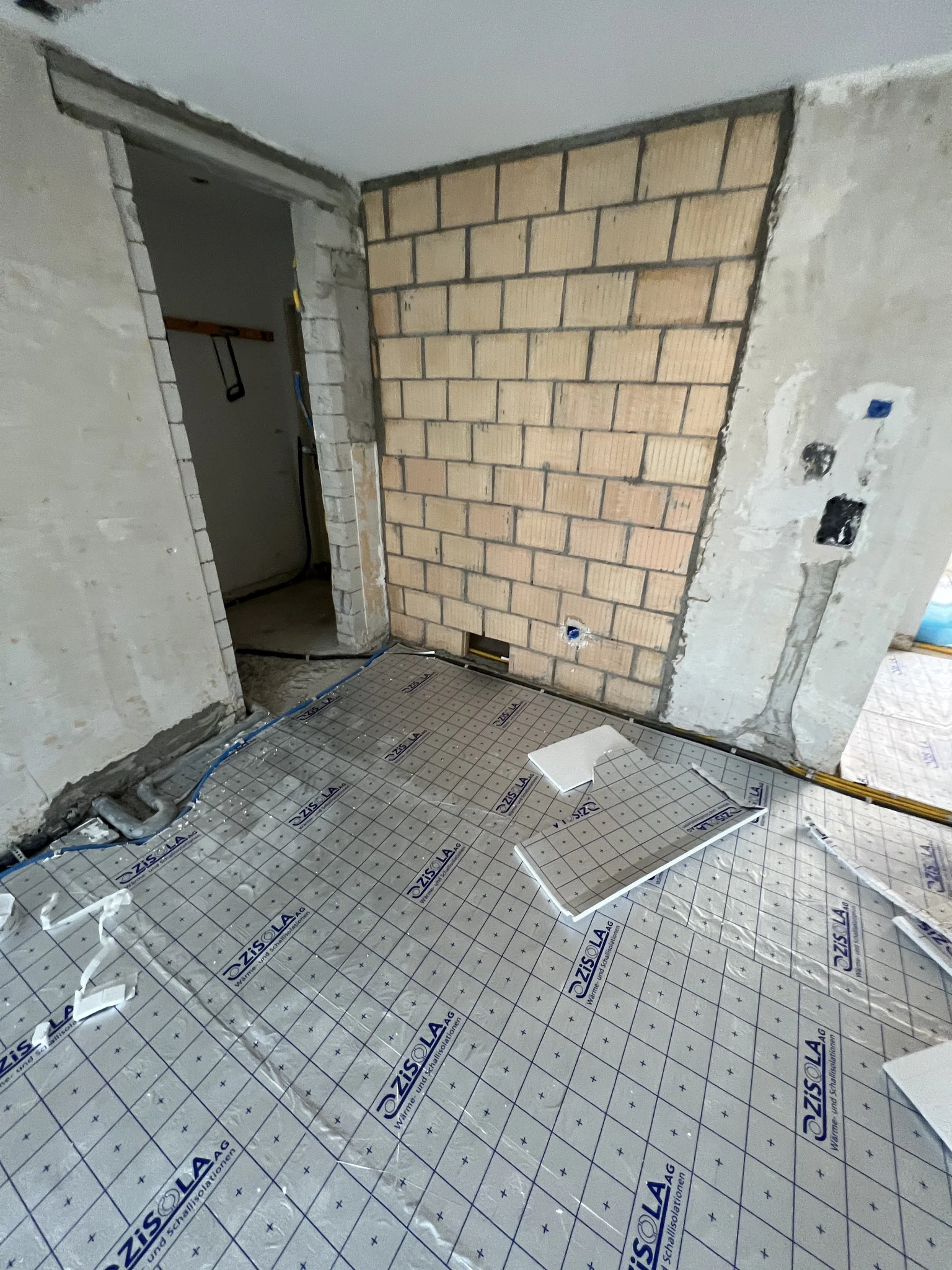 Neue Backsteinwand neben einer Türöffnung und vorbereiteter Bodenaufbau während des Umbaus