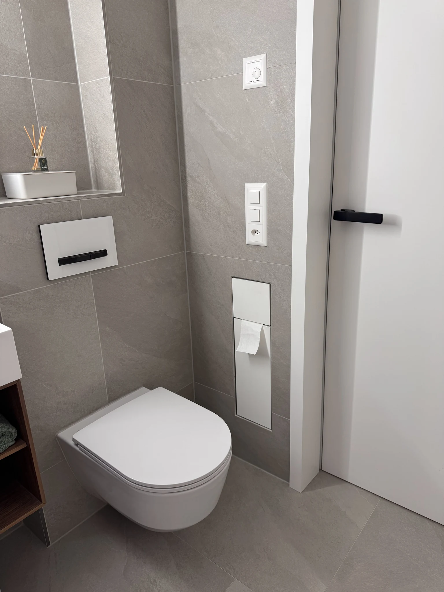 Wandhängendes WC mit Unterputzspülkasten und grauen Wand- und Bodenfliesen